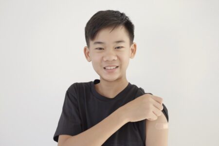 Mixed Asian teen boy showing his arm with bandage after being vaccinated