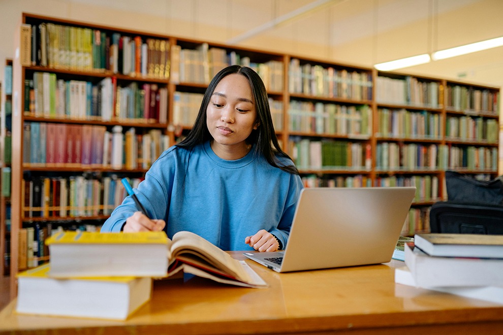 Funding for the Future teen taking notes in library with laptop