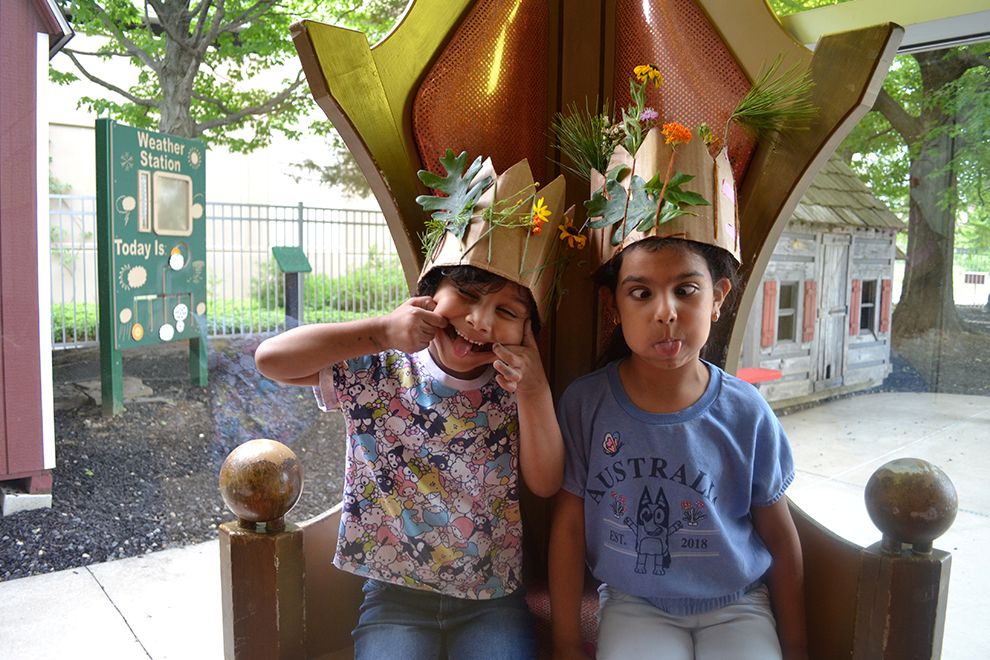two kids making silly faces and showing off their crafted crowns made from items found in nature