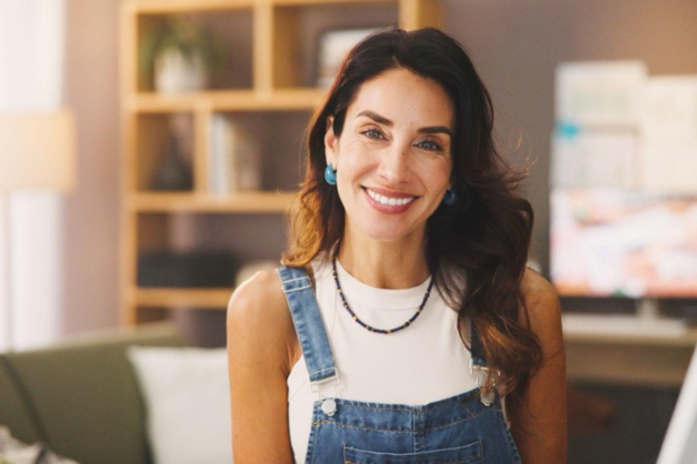 A woman with long dark hair wearing overalls and a white tank top