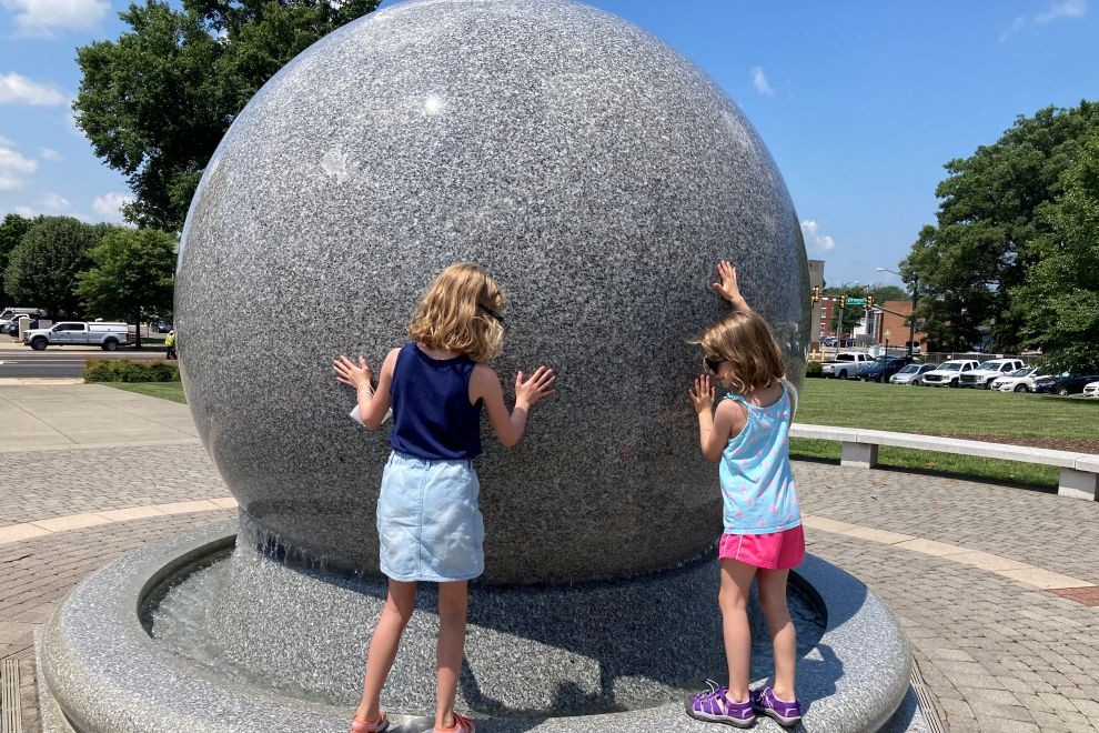 two girls playing on the Mary Morton Parsons Earth Kugel at Science Museum of Virginia